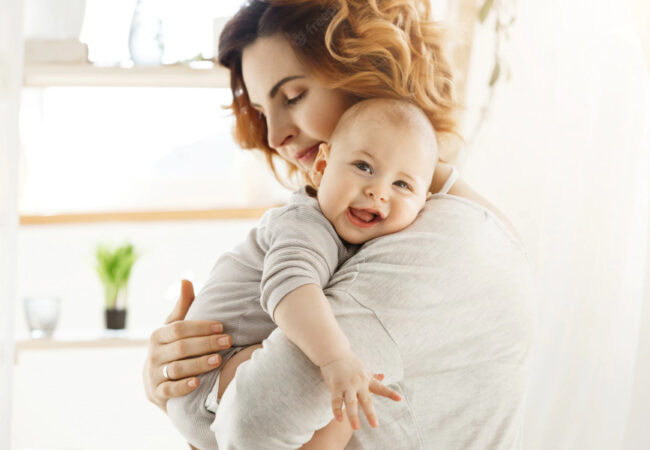 Mãe abraçada com seu bebê que está sorrindo e olhando para a foto